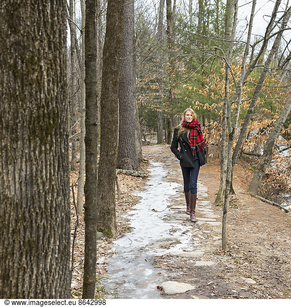 A woman in a winter coat and red scarf walking down a woodland path  in winter.