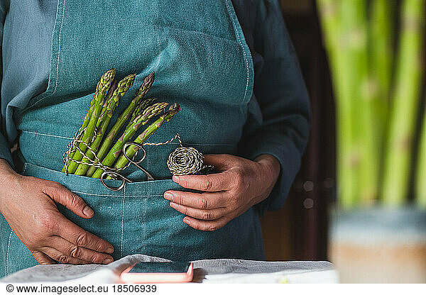 a woman in an apron will cook asparagus and reads a recipe