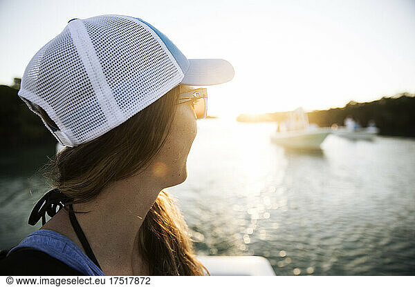 A woman in hat and sunglasses looks toward boats in the sun