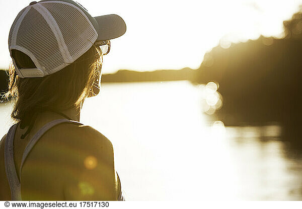 A woman in hat and sunglasses looks toward warm sunlight on the water