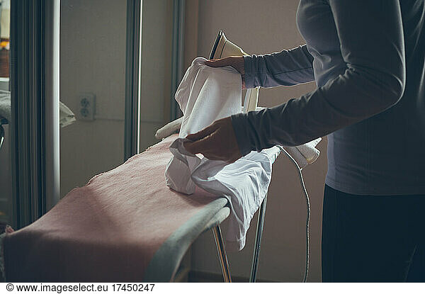 A woman irons clothes on an ironing board