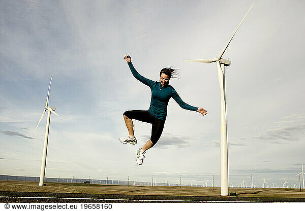 A woman jumping in the air with windmills in the background.