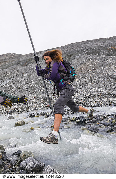 A woman jumps over a swift glacial stream with the aid of a pole near Gulkana Glacier  Alaska  United States of America