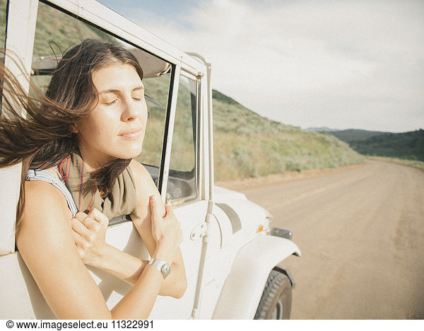 A woman leaning out of a moving jeep on a mountain road.