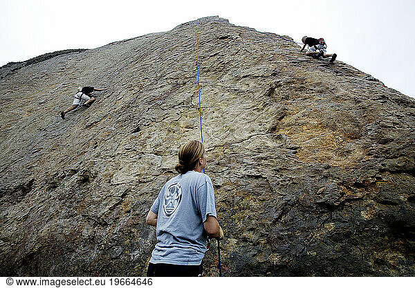 A woman looks on as two boys climb a rock wall in Malibu  California.