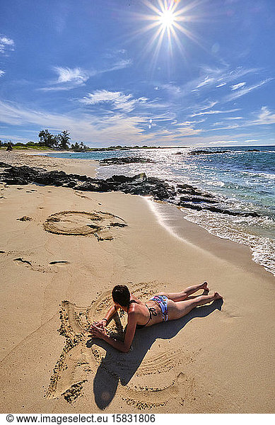 A woman make figures in the sand on Makalawena Beach  Hawaii