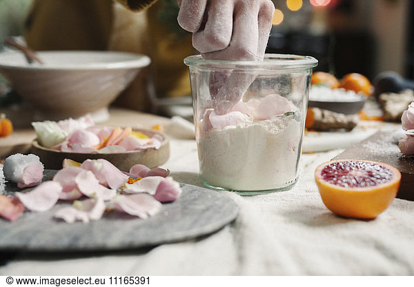 A woman mixing ingredients in a pot  sugar  oranges  petals  and ginger.