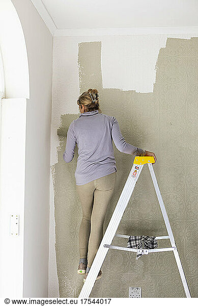 A woman on a ladder using a paint roller  decorating a room