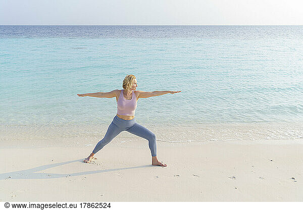 A woman on the beach does sports  yoga.