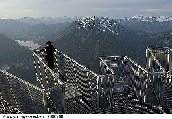 A woman on the 5 fingers lookout on Krippenstein mountain looks down on Hallstatt and Obertraun  Austria.