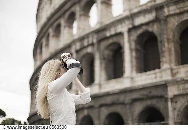 A woman outside the Colosseum amphitheatre in Rome  taking photographs.