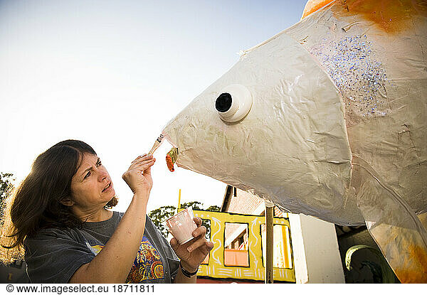 A woman painting fish lips for a parade in Santa Barbara. The parade features extravagant floats and costumes.
