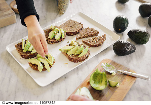 A woman preparing open sandwiches with brown bread and avocado.