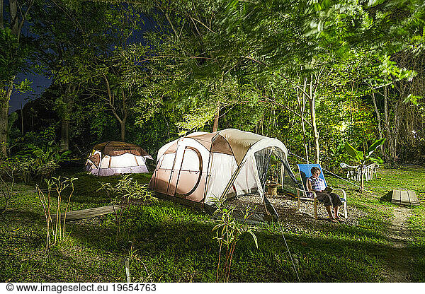 A woman reads a book at night in front of her tent at Rodney's Wellness Retreat on the Caribbean island of Dominica.