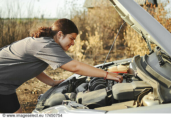 A woman repairs and troubleshoots a car outdoors on a bright sunny day