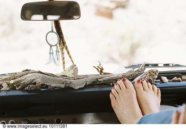 A woman resting her bare feet on the dashboard of a 4x4  on a road trip