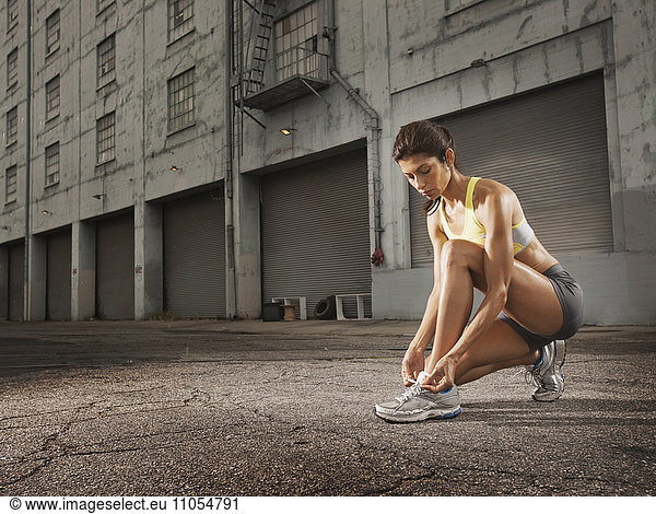 A woman runner leaning down and tying her running shoes laces.