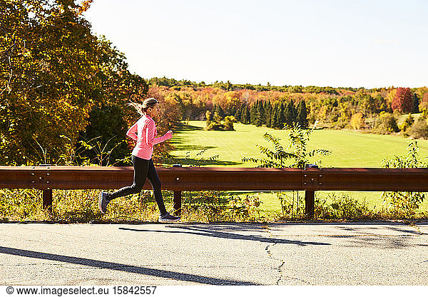 A woman running down a country road on a fall day.