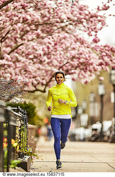 A woman running down a street in Boston  MA past a flowering tree.