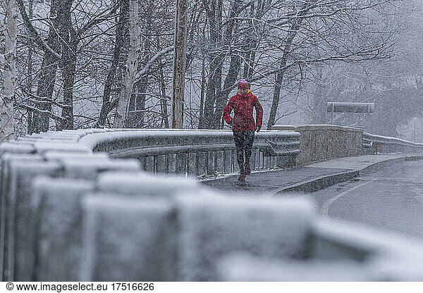 A woman running on a sidewalk during a snowstorm.