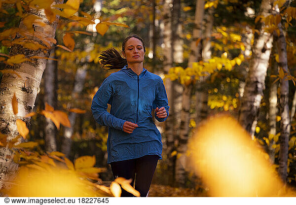A woman running on a trail in a forest of yellow leaves