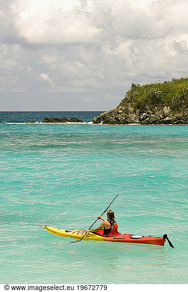 A woman sea kayaking past Cinnamon Cay in Virgin Islands National Park  St. John.
