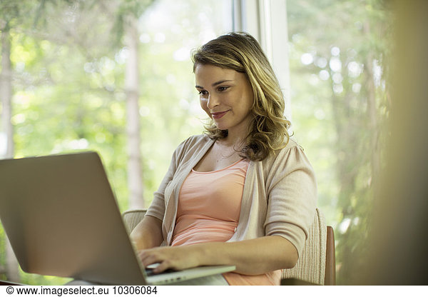 A woman seated using a laptop sitting on a verandah.