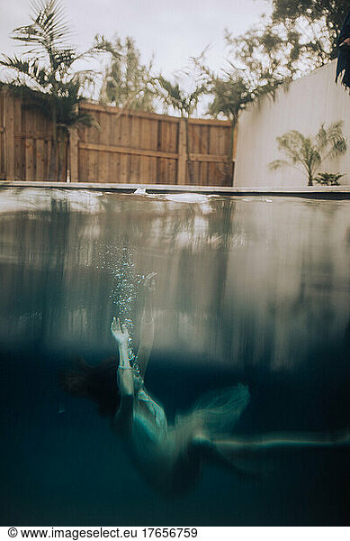 A woman sinking in a pool under glassy water