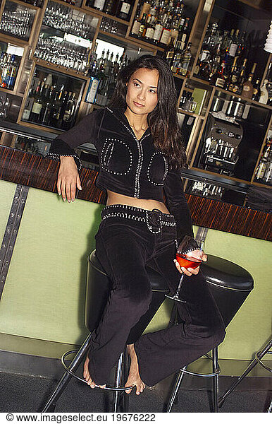 A woman sits at a bar with a drink.
