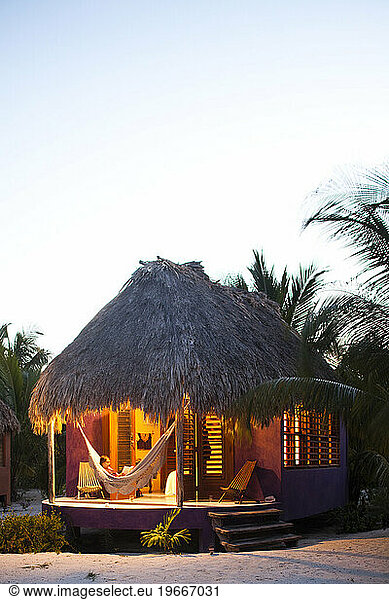 A woman sits in a hammock on the porch of her thatch cabana at a luxury hotel in Belize.