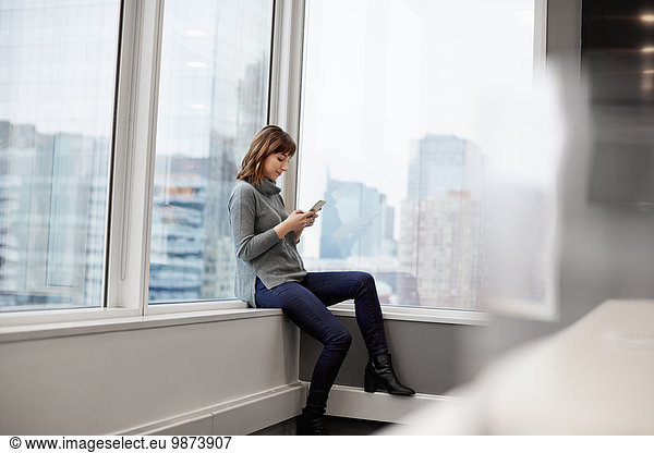 A woman sitting along  using a smart phone.
