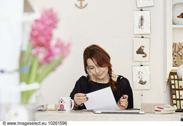 A woman sitting at a desk in a small gift shop  doing the paperwork  managing the business. A laptop on the desk.