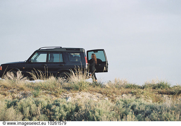 A woman standing by the open rear door of a 4x4 in open space.