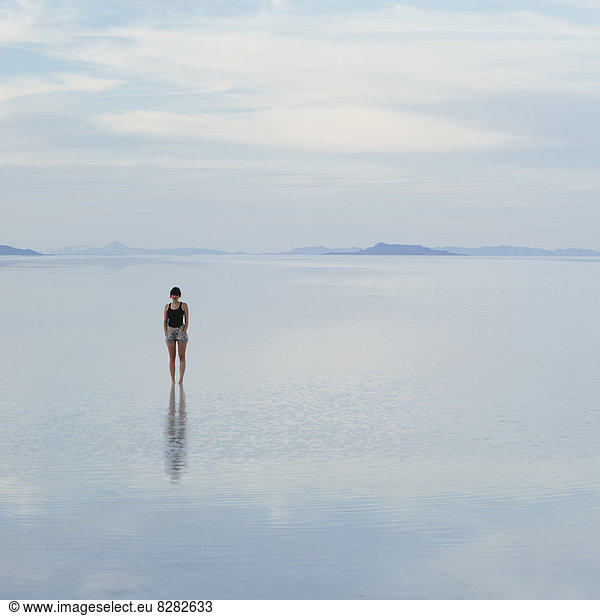 A Woman Standing On The Flooded Bonneville Salt Flats  At Dusk.