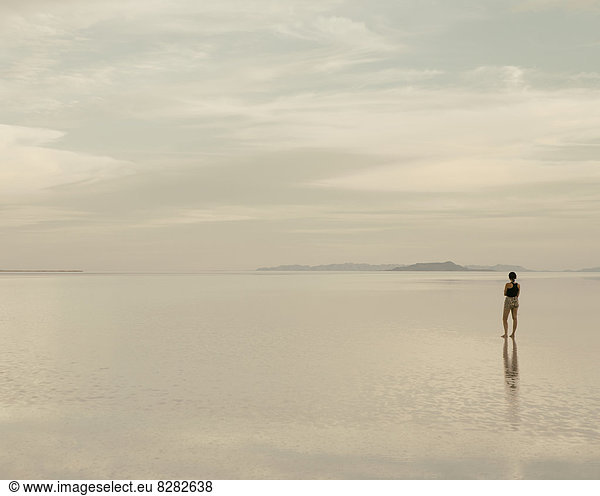 A Woman Standing On The Flooded Bonneville Salt Flats At Dusk. Reflections In The Shallow Water.