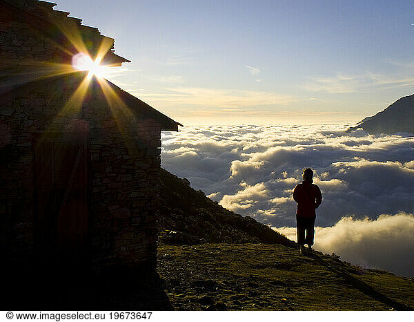 A woman standing taking in the view above the clouds next to a building while trekking in Nepal.
