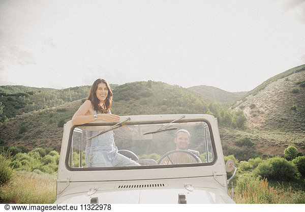 A woman standing up in an open top jeep in the mountains.