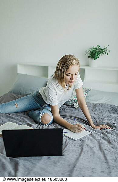 a woman studies sitting on a bed with a laptop