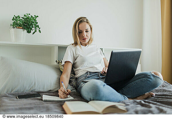 a woman studies sitting on a bed with a laptop