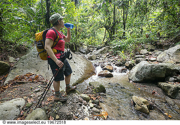 A woman takes a water break by a stream on her hike of Segment 3 of the Waitukubuli National Trail on the Caribbean island of Dominica.