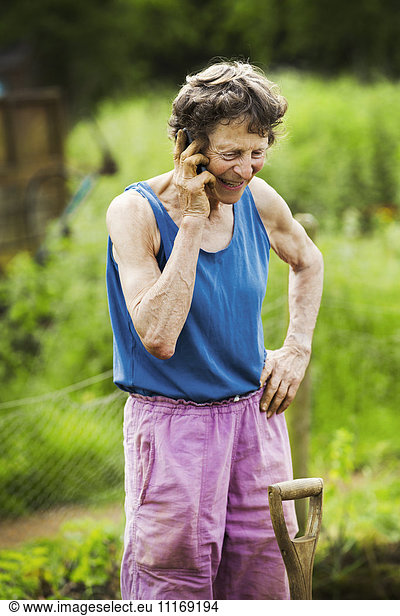 A woman talking on the phone with a shovel by her leg in a farm.