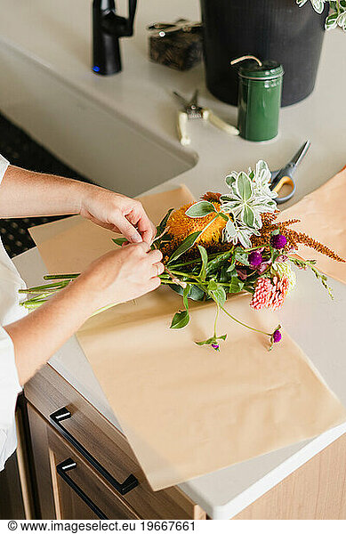 A woman tying a bouquet of fall flowers together on her kitchen