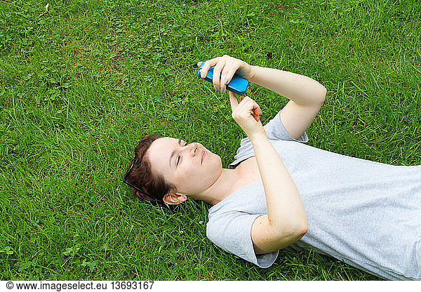 A woman uses her iPhone on the grass outdoors.