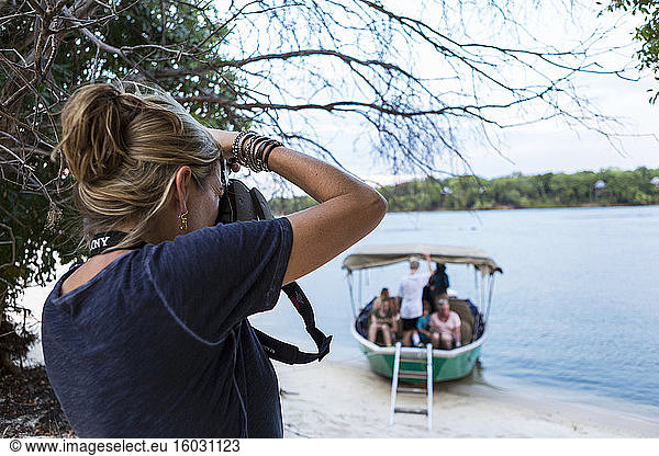 A woman using her camera  taking photographs of a boat with passengers on the Zambezi River  Botswana
