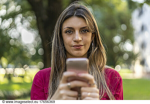 A woman using her smartphone outdoors. She is looking at the camera.