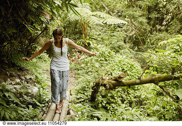 A woman walking carefully across a bamboo bridge in the jungle.