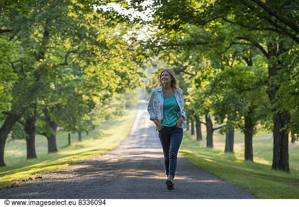 A woman walking down a tree lined path.