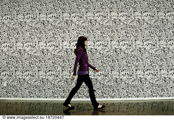 A woman walking in front of a busy wall.