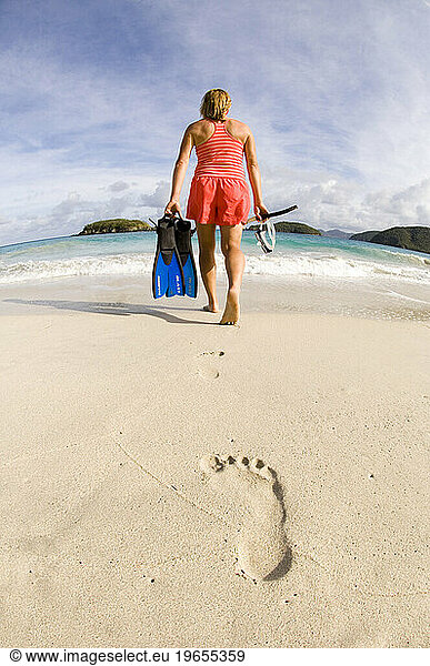 A woman walking on Cinnamon Bay beach with snorkeling gear in Virgin Islands National Park  St. John.