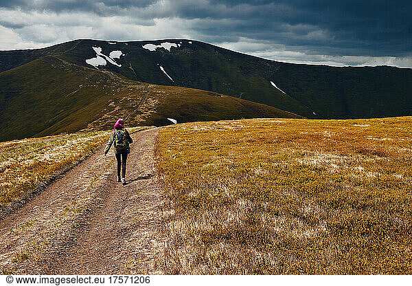 A woman walks along a mountain path along a mountain range.